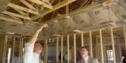 Two businessmen stand inside a scaffolded home. One is gesturing toward the roof structure.