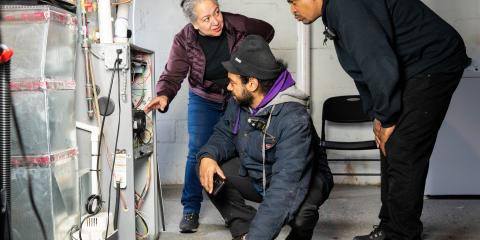 Three people observing an indoor heating unit.